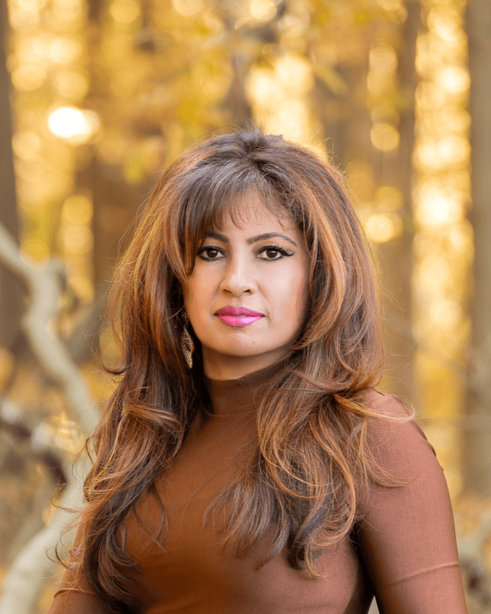 Jothi Moorthy headshot, brown outfit, autumn forest
